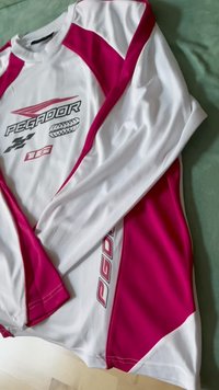 Dugi rukav sportska majica u bijeloj boji s ružičastim panelima. Sadrži naziv branda "PEGADOR" i logotip. Materijal izgleda lagano i glatko.
