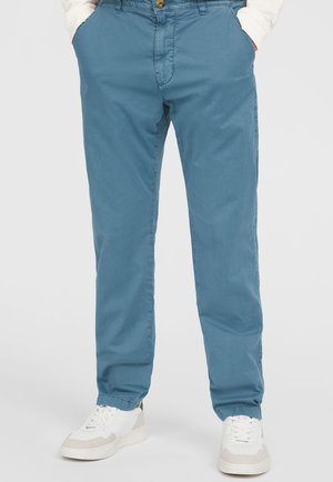 Light blue cotton trousers with a relaxed fit, featuring side pockets and a button closure, paired with white and beige sneakers.