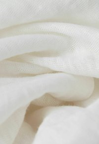 Tessuto bianco, morbido e leggero, presenta una texture a maglia fine con leggere variazioni nella trama. Il materiale appare liscio con una caduta delicata.