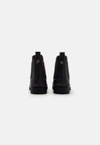 Botas de borracha pretas até ao tornozelo com painéis laterais em elastano, sola resistente e laço na parte traseira. Logótipo visível no lado exterior.