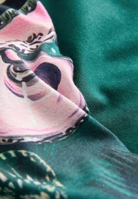 Zöld háttérrel rendelkező szövet, amelyen rózsaszín és lila absztrakt mintázat látható, sima textúrával és bonyolult mintákkal.