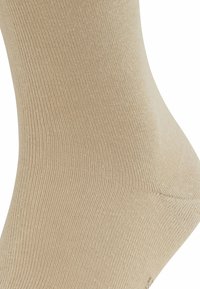 Calzino in cotone beige con texture a coste, superficie liscia e forma sagomata. Nessun motivo evidente o dettagli hardware.