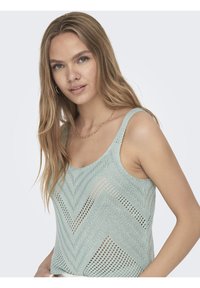 Débardeur en tricot vert menthe avec un motif en chevron, des bretelles larges et une coupe décontractée, présentant un fil texturé avec des détails de points ouverts.