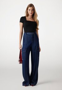 Top nero attillato con scollatura quadrata, abbinato a pantaloni in denim scuro a gamba larga e vita alta, con tasche frontali e cintura.