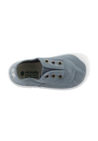 Zapato slip-on de lona gris claro con suela de goma blanca, que cuenta con dos ojales metálicos y una textura suave. El interior incluye el logo de la marca.