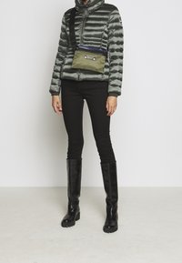 Vadderad, iriserande grå puffjacka med hög krage, kombinerad med svarta jeans och knähöga svarta stövlar. Olivgrön axelväska med blå dragkedja.