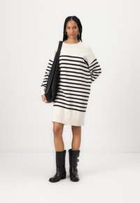 Knit dress featuring cream and navy stripes, relaxed fit, long sleeves. Paired with knee-high black boots and a black shoulder bag.