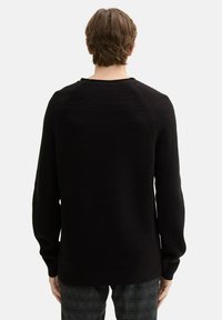 Schwarzer Strickpullover mit strukturierter Musterung, geripptem Saum und langen Ärmeln. Von der Rückseite auf einem neutralen Hintergrund präsentiert.
