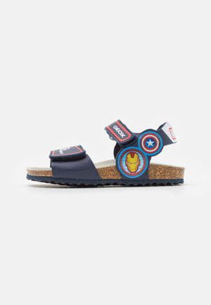 Marineblå sandal med justerbare stropper, korksål og Iron Man grafiske detaljer. Har velcro-lukninger og en tekstureret ydersål.