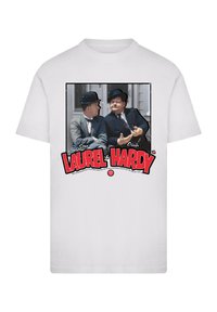 White cotton t-shirt featuring a printed image of two men in bowler hats, with "Stan Laurel & Oliver Hardy" in bold red letters below.