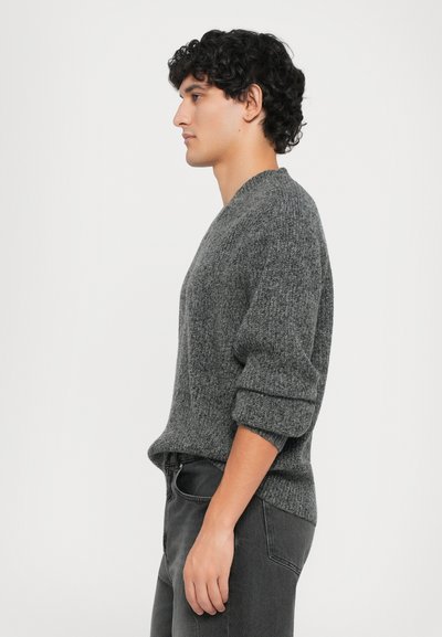 Gray knitted sweater with a round neckline and rolled sleeves, paired with dark jeans, shown from the side against a white background.