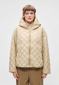 Μπεζ �καπιτονέ μπουφάν με κουκούλα, που διαθέτει εμπρόσθιο φερμουάρ και πλαϊνές τσέπες. Το υλικό έχει λεία υφή και ελαφρύ σχεδιασμό.