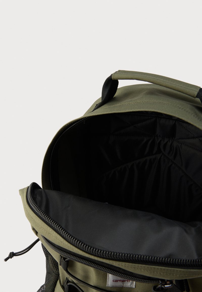 Olivgrüner Rucksack mit schwarzem Innenfutter, Reißverschlussöffnung und oberem Griff. Merkmale sind eine Netz-Seitentasche und gepolstertes Innenfutter.