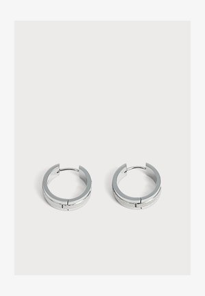 Paire de petites boucles d'oreilles en argent en forme de créoles avec un motif subtilement texturé, placées sur un fond clair uni.