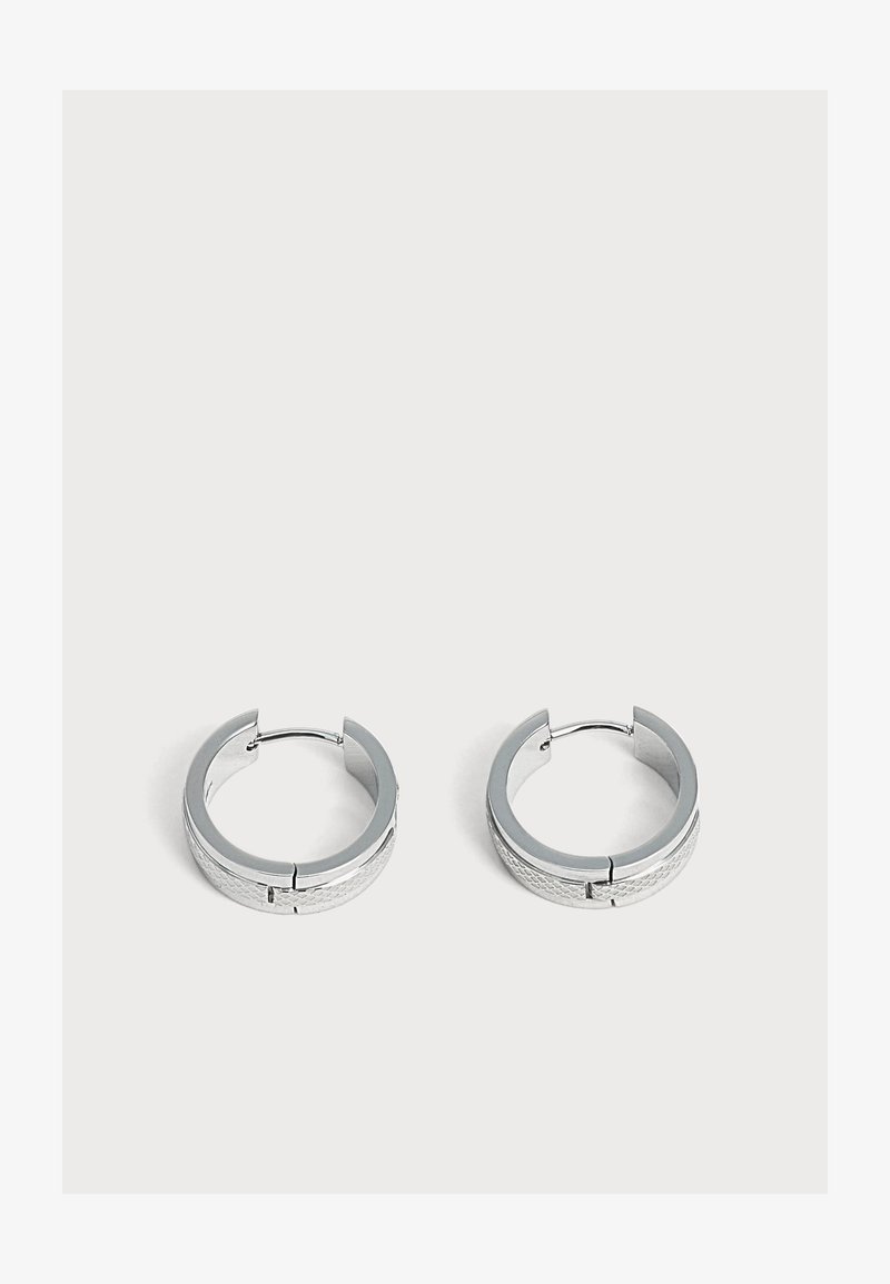 Paire de petites boucles d'oreilles en argent en forme de créoles avec un motif subtilement texturé, placées sur un fond clair uni.
