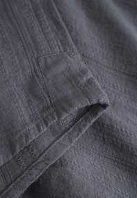 Gray textured fabric with horizontal stripes, featuring a subtle pocket and frayed edges, made from a lightweight material.
