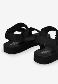 Sandalias de plataforma negras con correas de nylon ajustables y suela de goma texturizada. El diseño enfatiza la comodidad con una estética minimalista.