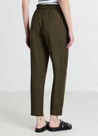 Pantaloni verde oliva con vita elastica, vestibilità comoda, gambe affusolate e tessuto liscio, abbinati a sandali neri a ciabatta con decorazioni.