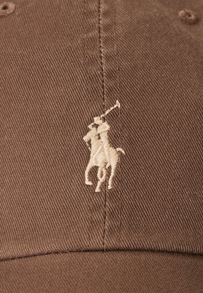 Ruda audinio kepuraitė su smėlio spalvos siuvinėtu logotipu, vaizduojančiu polo žaidėją ant arklio, laikantį lazdelę.