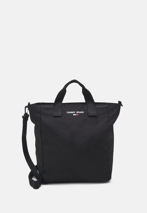 Czarna torba typu tote Tommy Jeans z górnymi uchwytami i regulowanym paskiem na ramię na jednolitym jasnym tle.