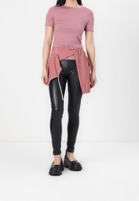 Růžový top s krátkým rukávem, černé legíny z umělé kůže, červená a bílá kostkovaná košile uvázaná v pase a robustní černé boty.