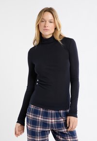 Dolcevita nera a maniche lunghe, aderente, realizzata in tessuto morbido. Abbinata a pantaloni da pigiama a quadri blu con accenti rossi e bianchi.