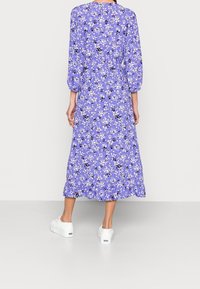 Violet kukka-mekko, jossa on kolmannes hihoja puffi-muotoilulla, röyhelöhelma ja valkoiset lenkkarit. Mekossa on satunnaisia valkoisia, keltaisia ja mustia kukkakuosisia kuvioita.