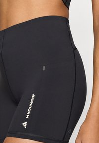 Μαύρο αθλητικό σορτς από ελαστικό ύφασμα, με εφαρμοστή σχεδίαση, λεία υφή, λευκό λογότυπο σε αντίθεση και λεπτομερείς ραφές.