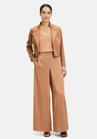 Tan faux leren jasje met een reverskraag, gecombineerd met een bijpassend tanktop en wijde broek. Glad textuur, minimale accenten.