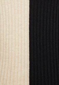 Rippenstrickstoff vertikal geteilt; eine Seite cremefarben-beige, die andere tiefschwarz. Die Textur wirkt weich und warm mit schmalen Rippen.