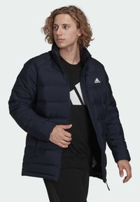 Giacca puffer blu marino con texture a righe orizzontali, cerniera completa, colletto alto e logo ricamato bianco sul lato sinistro del petto.