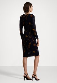 Långärmad, figursydd klänning i marinblått med guld- och röda blommönster, knälång. Kombinationen med svarta högklackade sandaler. Slät textur.