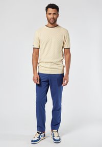 Suéter de punto texturizado en crema de manga corta con ribete negro, combinado con pantalones azules y zapatillas en azul y blanco. Diseñado para un uso casual.