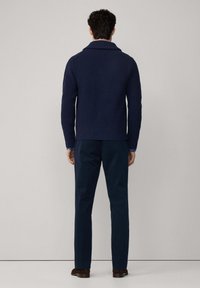Maglione a coste navy con colletto sciallato, abbinato a pantaloni scuri e scarpe marroni. Il maglione presenta un design aderente e un tessuto testurizzato.