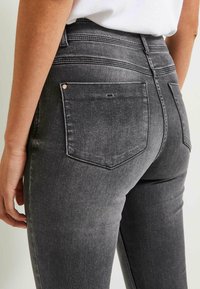 Höga grå denimjeans med bakfickor, diskret slitningar och sydda detaljer längs midjan.