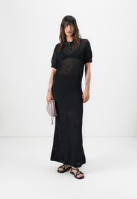 Rochia tricotată neagră combină un top de stil polo cu o fustă lungă. Are un model texturat, mâneci scurte și o siluetă ajustată.