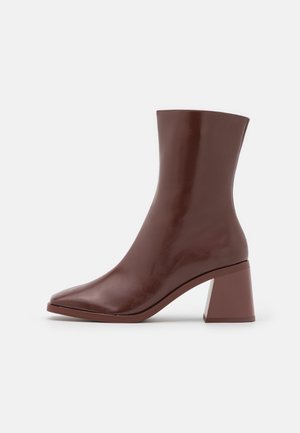 Botte en cuir marron mi-mollet avec bout pointu et large talon bloc sur fond blanc.
