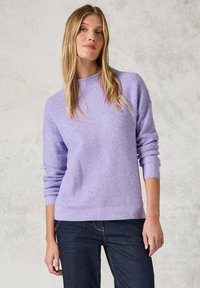 Pull en maille violet clair avec un motif texturé, col rond et poignets côtelés. Associé à un jean bleu foncé.