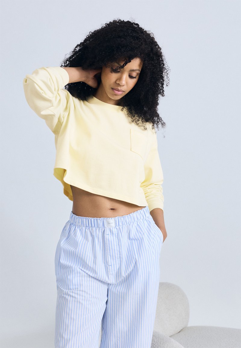 Κίτρινο κοντό τοπ με μακριά μανίκια και τσέπη στο στήθος, συνδυασμένο με ανοιχτό μπλε και άσπρο ριγέ, φαρδιά παντελόνια. Μαλακό ύφασμα και άνετη εφαρμογή.