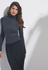 Langærmet, mørkegrå rullekrave i blødt, tekstureret materiale, kombineret med sorte bukser med elastisk taljebånd. Enkel, minimalistisk design.