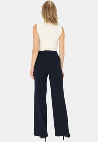 Granatowe spodnie z szerokimi nogawkami, wykonane z gładkiego materiału, z wysokim stanem i długim krojem, zapewniające luźny fason. Udekorowane subtelnymi szwami.