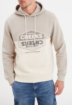 Sudadera con capucha en beige y crema con un bolsillo canguro frontal y estampado gráfico. Presenta cordones y puños acanalados para un ajuste adecuado.