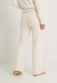 Suéter esponjoso de color crema y pantalones de pierna ancha hechos de material suave. Los pantalones tienen un ajuste relajado con bordes sin rematar en los puños.