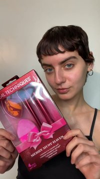 Set regalo Real Techniques Merry Must-Haves in una scatola di plastica trasparente, con spugnette per il trucco rosa e rosse e un pennello per il blush, legati con un fiocco.