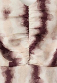 Gros plan d’un tissu avec couture centrale froncée et motif tie-dye abstrait marron et beige sur un matériau texturé.