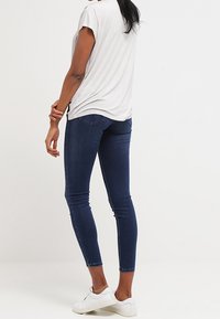 Hedké tmavě modré džíny s mírným vyblednutím, kombinované se světle šedým tričkem. Oblečení doplňují bílé tenisky.