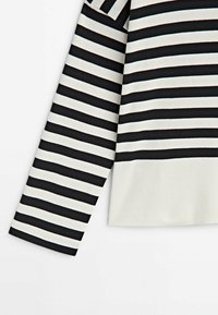 Pitkähihaisessa paidassa on mustavalkoisia vaakaraitoja, ja se näyttää hihaa ja alavatsaa valkoisella taustalla.