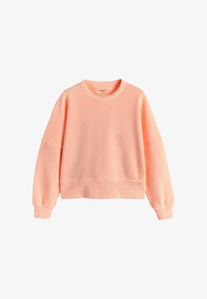 Mīksts persiku krāsas džemperis ar garām piedurknēm, ribveida aprocēm un vidukļa daļu, izklāts uz balta fona.