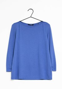 Blå langærmet bluse med rund halsudskæring, side-slids, lavet af tekstureret stof. Den hænger på en sort bøjle mod en hvid baggrund.