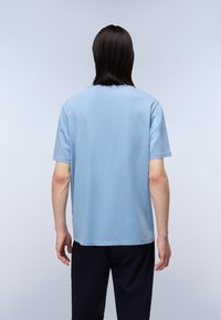 Světle modré bavlněné tričko s krátkými rukávy, měkkou texturou a volným střihem. Má kulatý výstřih a rovný lem, bez viditelných log.